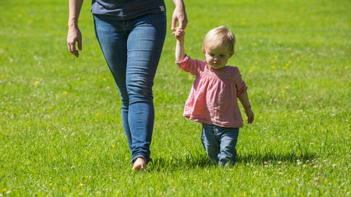 A toddler holding an adult's hand walks on grass through the garden at Godolphin, Cornwall